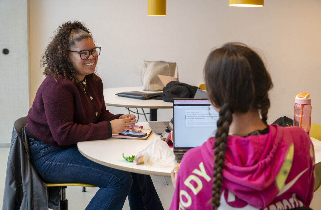 Twee studenten in gesprek aan een tafel in een onderwijsgebouw